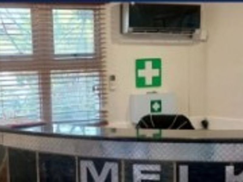 A functional office reception area featuring a built-in reception desk, wall-mounted air conditioning unit, and window blinds.
