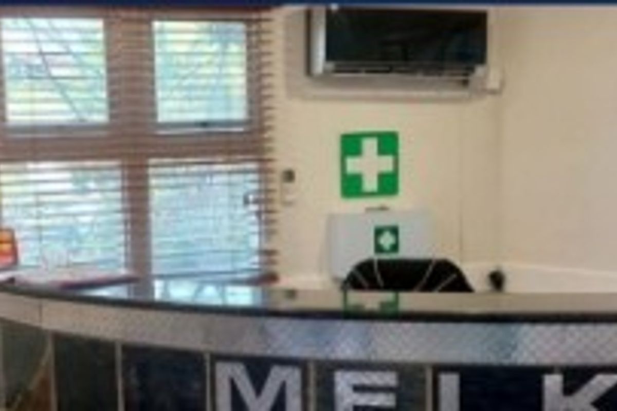 A functional office reception area featuring a built-in reception desk, wall-mounted air conditioning unit, and window blinds.