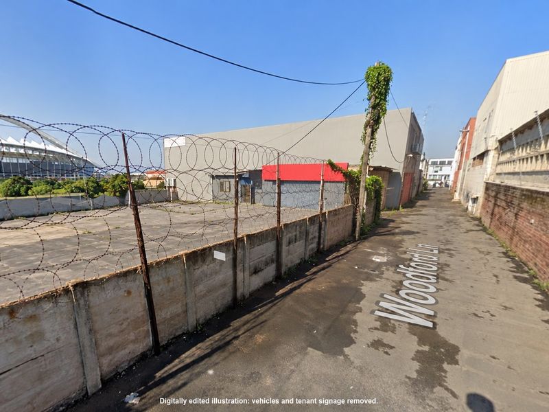 Street view of a commercial property access lane featuring a concrete boundary wall with razor wire security fencing.