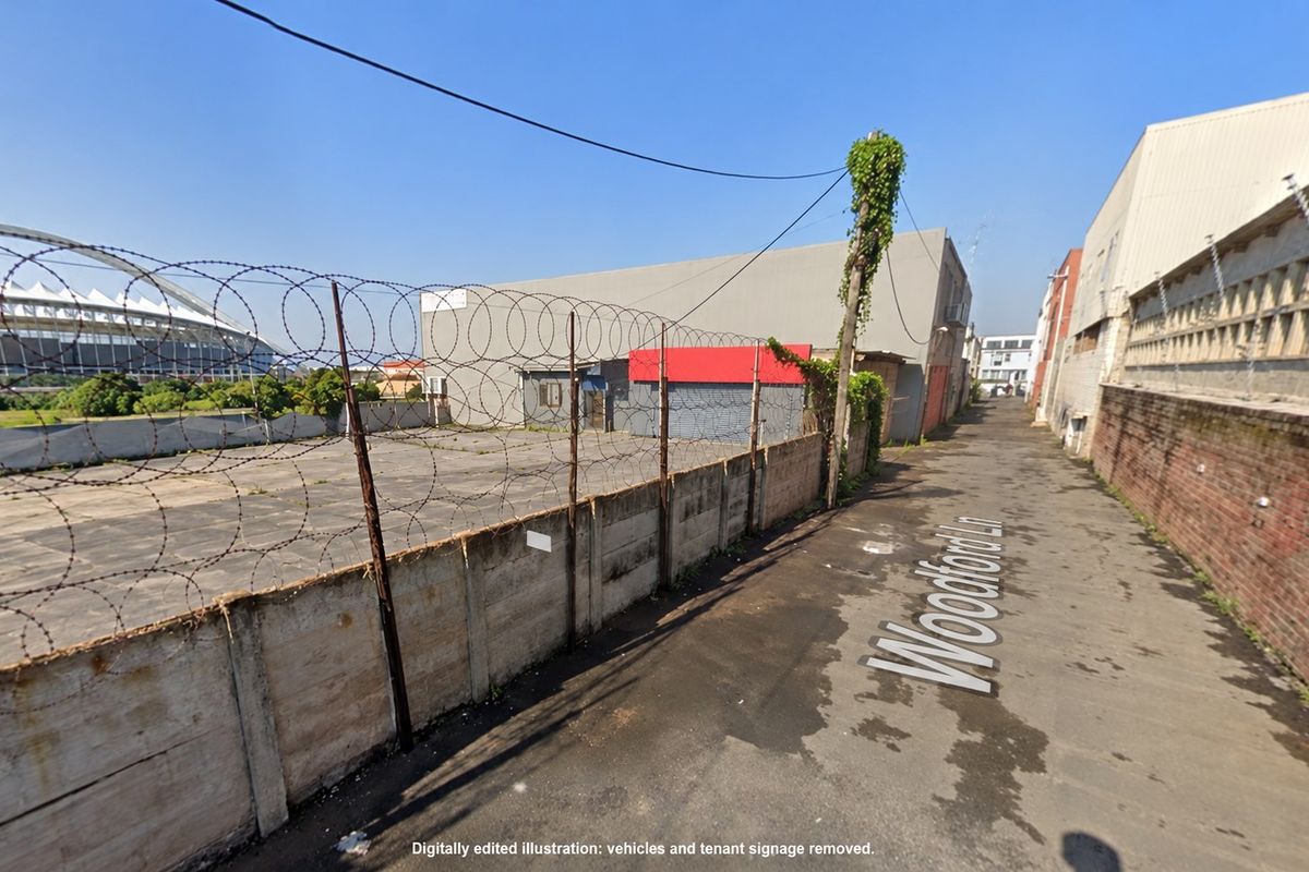 Street view of a commercial property access lane featuring a concrete boundary wall with razor wire security fencing.