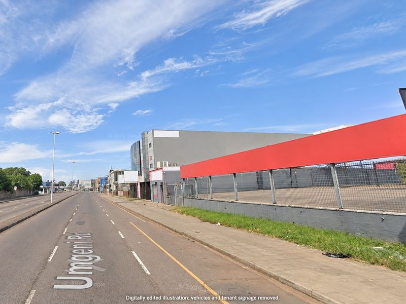 Street view of the commercial property frontage featuring a perimeter fence, retaining wall, and paved sidewalk along the main road.
