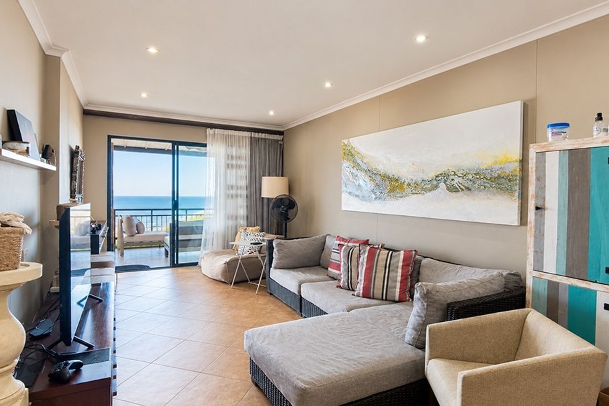 A bright living room featuring tiled flooring, recessed downlights, and a large sliding glass door providing access to a balcony with ocean views.