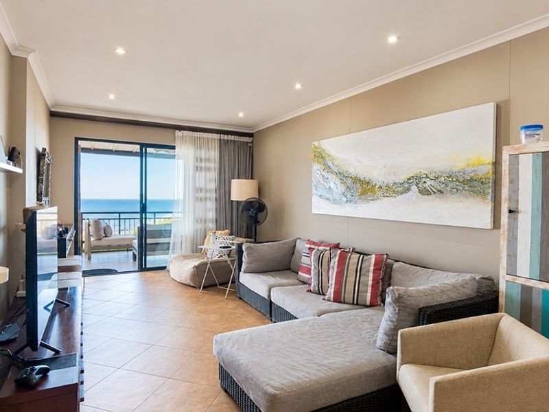 A bright living room featuring tiled flooring, recessed downlights, and a large sliding glass door providing access to a balcony with ocean views.