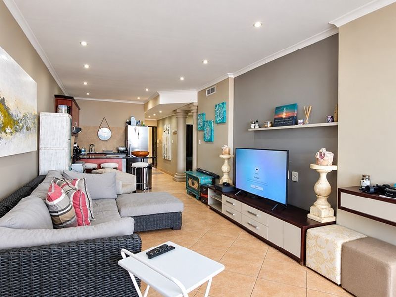 Open-plan living area featuring tiled floors, recessed lighting, and a functional kitchen with a breakfast counter, seamlessly connecting to the lounge space.