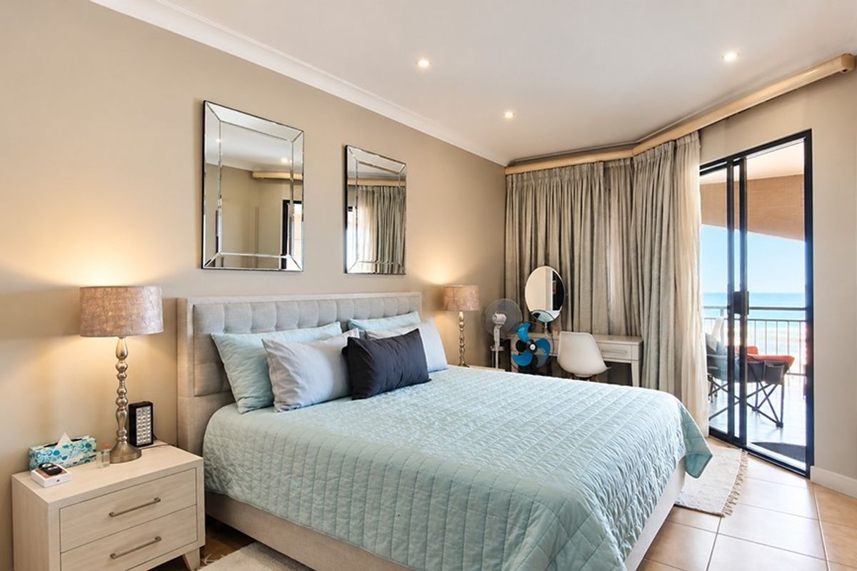 A well-maintained bedroom featuring tiled flooring, recessed downlighting, and direct access to a private balcony with ocean views.