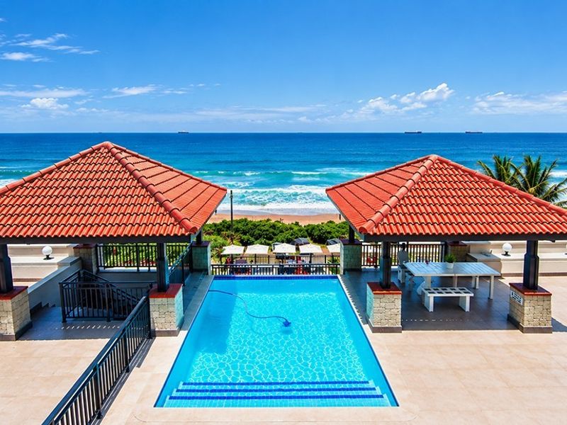 An elevated outdoor pool area featuring two covered gazebos with terracotta roofing, overlooking the ocean with direct beach access.