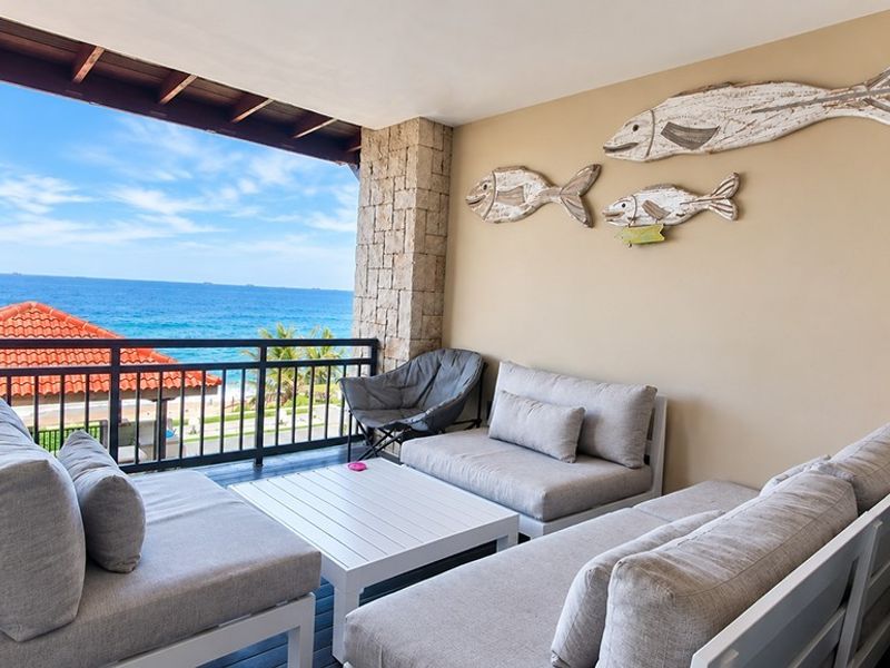 A spacious covered balcony featuring stone cladding, timber ceiling beams, and a metal balustrade, offering expansive ocean views.