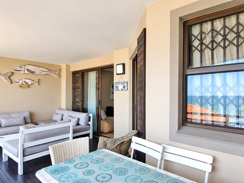 A spacious covered balcony featuring timber decking, sliding glass doors, and security gates, offering a comfortable outdoor living area.