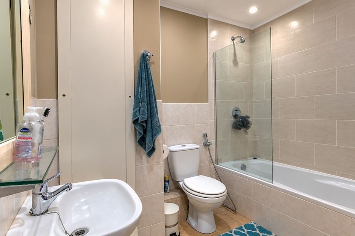 A well-maintained bathroom featuring a built-in bathtub with a glass shower screen, ceramic wall tiling, and a modern vanity basin.