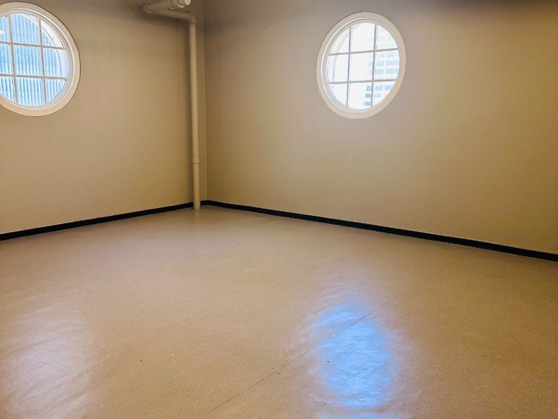 An empty, well-maintained office space featuring exposed ceiling beams, industrial-style lighting, fire sprinkler systems, and distinctive circular windows with polished epoxy flooring.