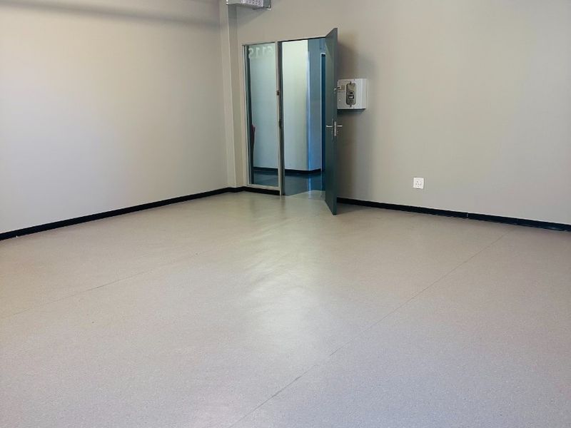 A clean, vacant office space featuring neutral walls, durable vinyl flooring, exposed industrial-style fire sprinkler piping, and an integrated intercom system.