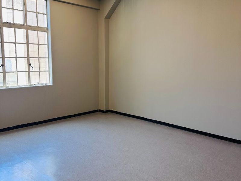 A bright, empty office space featuring industrial-style steel-framed windows, exposed concrete ceilings, and durable vinyl flooring, suitable for a professional workspace.