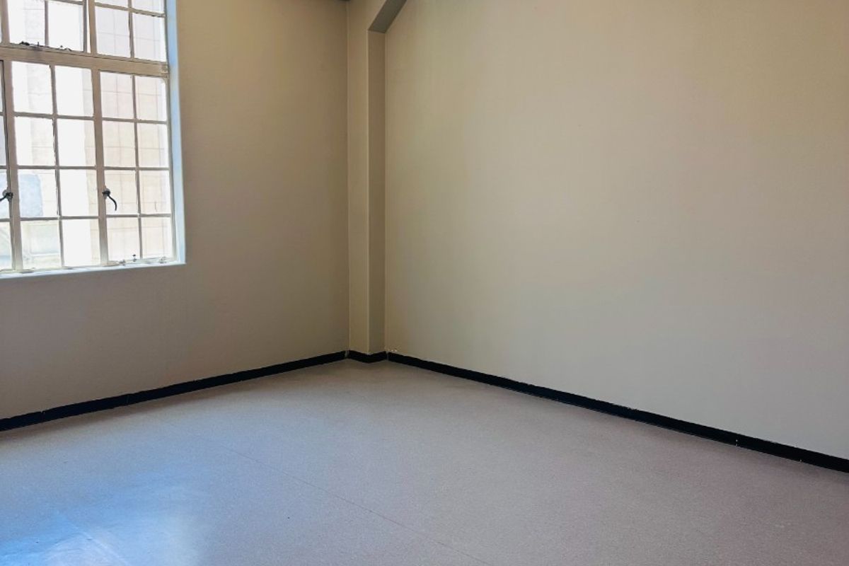 A bright, empty office space featuring industrial-style steel-framed windows, exposed concrete ceilings, and durable vinyl flooring, suitable for a professional workspace.