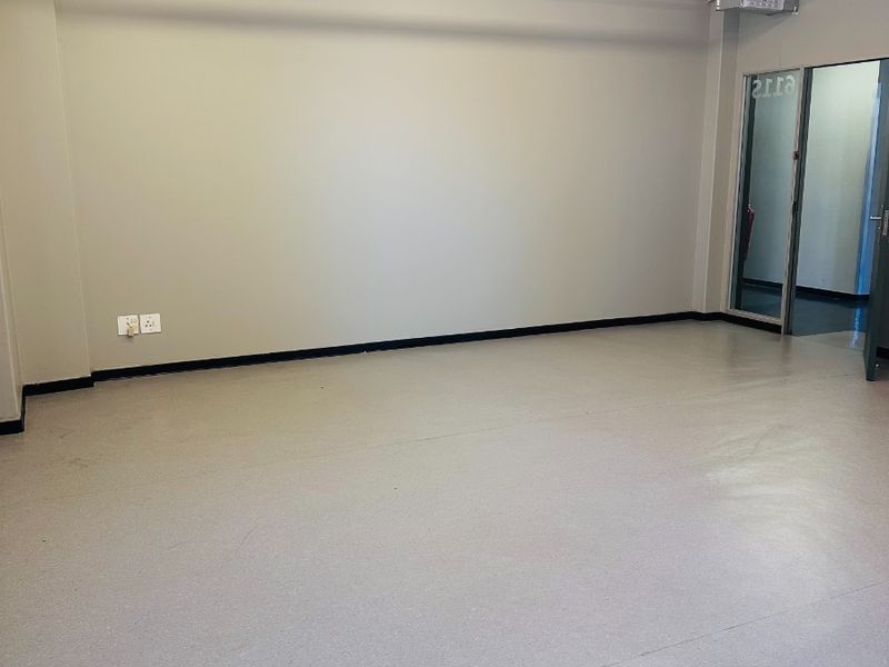 A clean, vacant office space featuring durable vinyl flooring, exposed fire safety infrastructure, and bright overhead fluorescent lighting.