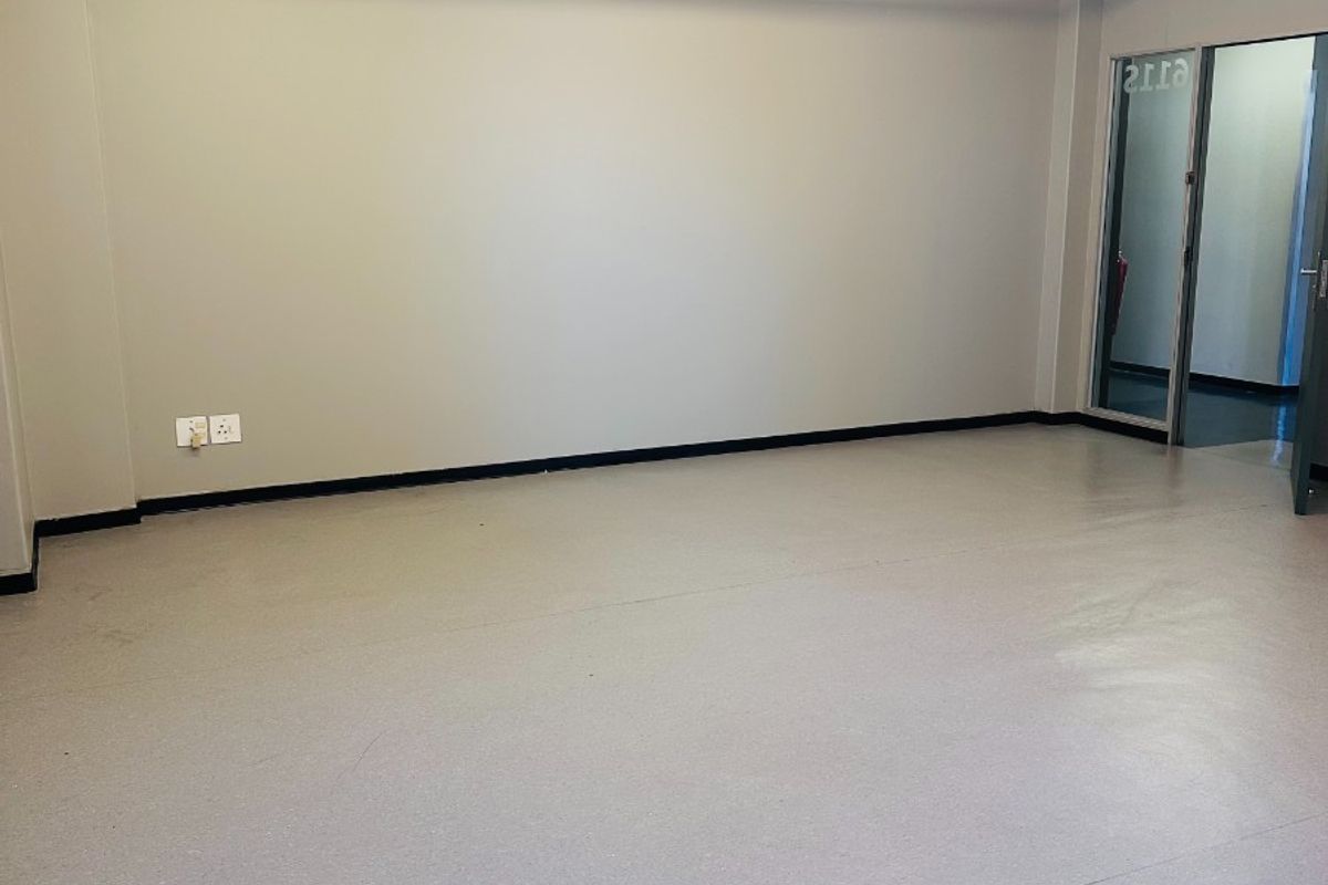 A clean, vacant office space featuring durable vinyl flooring, exposed fire safety infrastructure, and bright overhead fluorescent lighting.