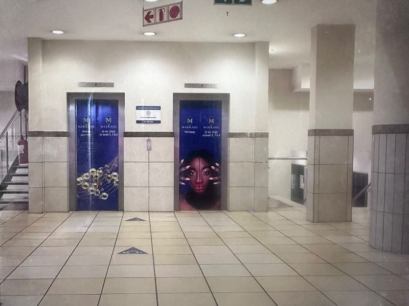 A commercial building hallway featuring two elevator banks with branded doors, tiled flooring, and recessed lighting.
