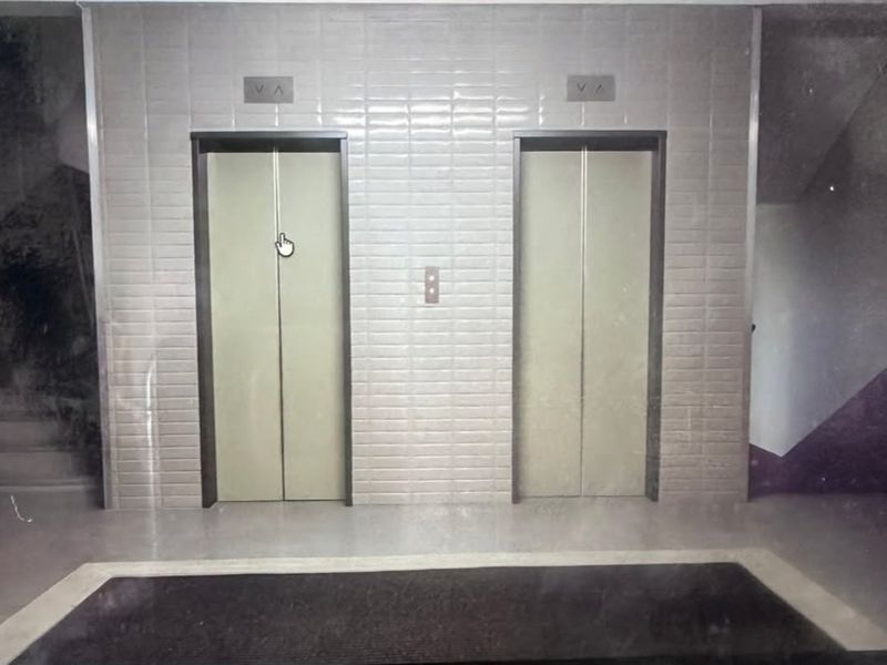 A commercial building elevator lobby featuring dual elevator doors and tiled wall finishes with adjacent stairwell access.