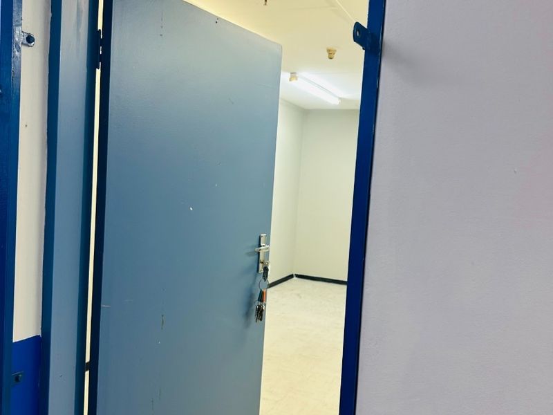 An empty office space featuring a blue painted door, neutral walls, and functional overhead lighting, suitable for a professional workspace setup.