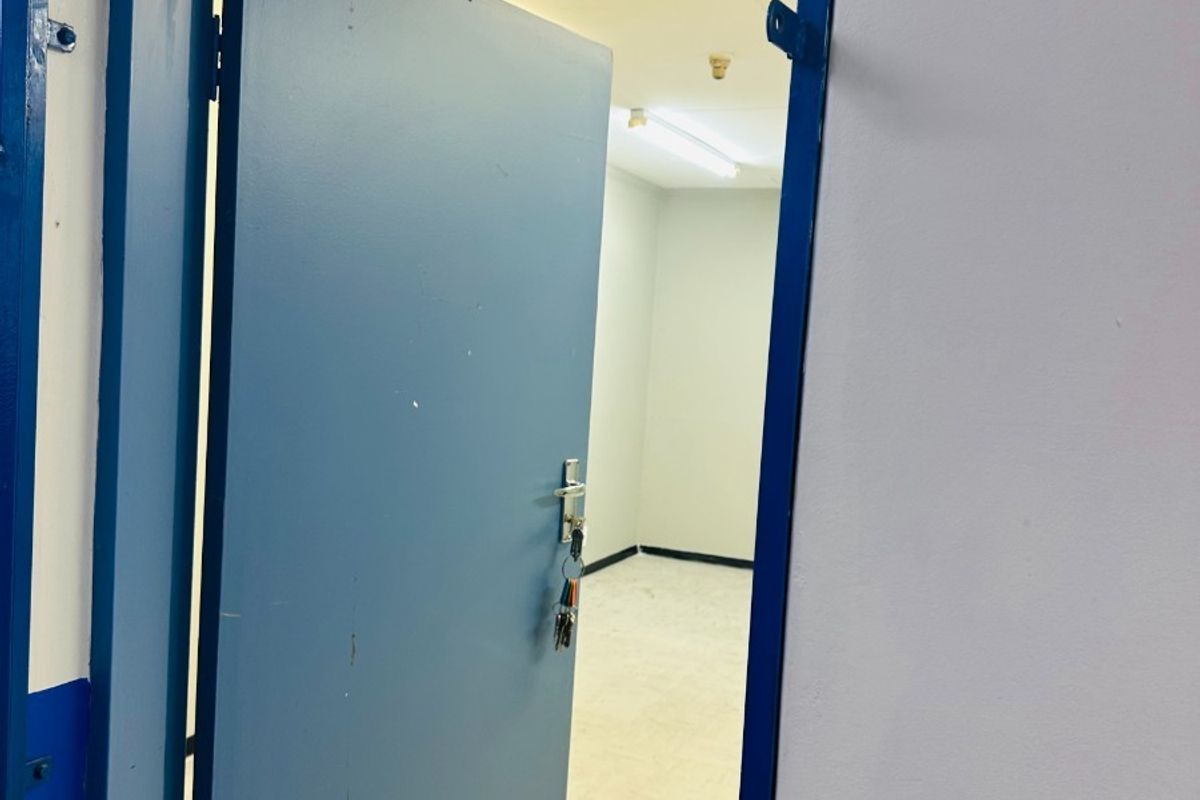 An empty office space featuring a blue painted door, neutral walls, and functional overhead lighting, suitable for a professional workspace setup.