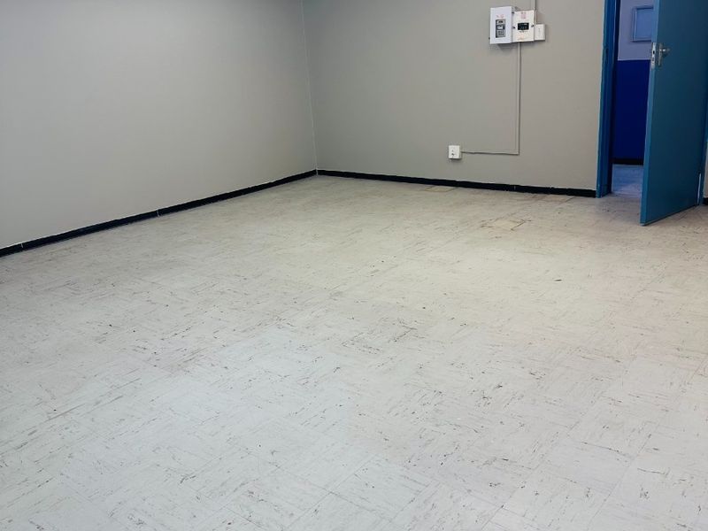 An empty office space featuring exposed ventilation ducting, fluorescent lighting, and durable vinyl floor tiles.
