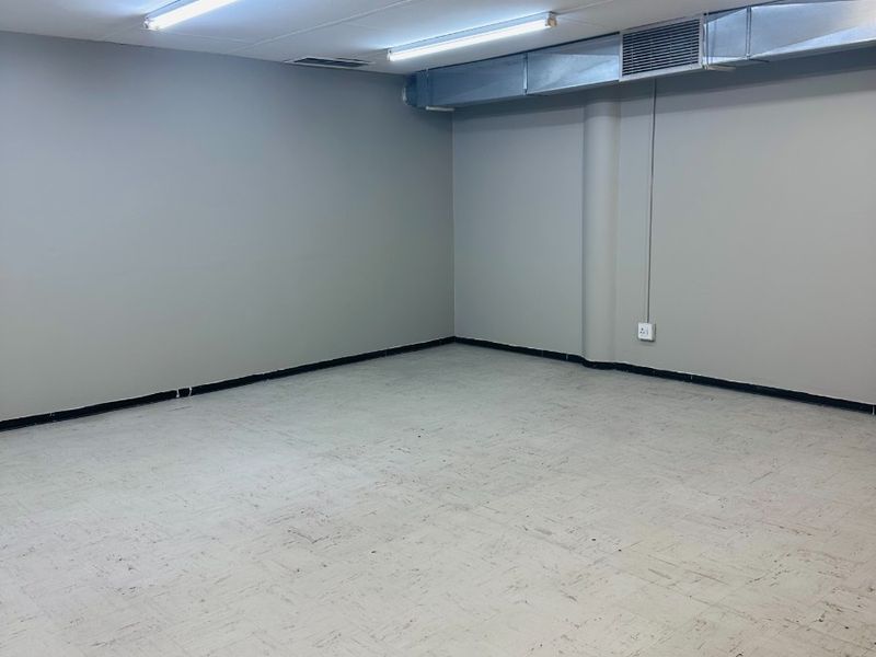 An empty, functional office space featuring exposed HVAC ducting, suspended ceiling tiles, and durable vinyl flooring, suitable for a variety of professional uses.