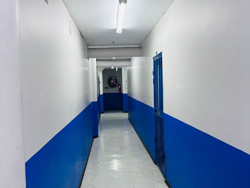 A functional commercial hallway featuring vinyl flooring, fluorescent lighting, and a security gate, presenting a utilitarian aesthetic suitable for office or industrial use.