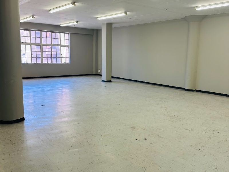 Spacious open-plan commercial office area featuring structural columns, vinyl flooring, and fluorescent lighting, offering a versatile blank canvas for various business configurations.