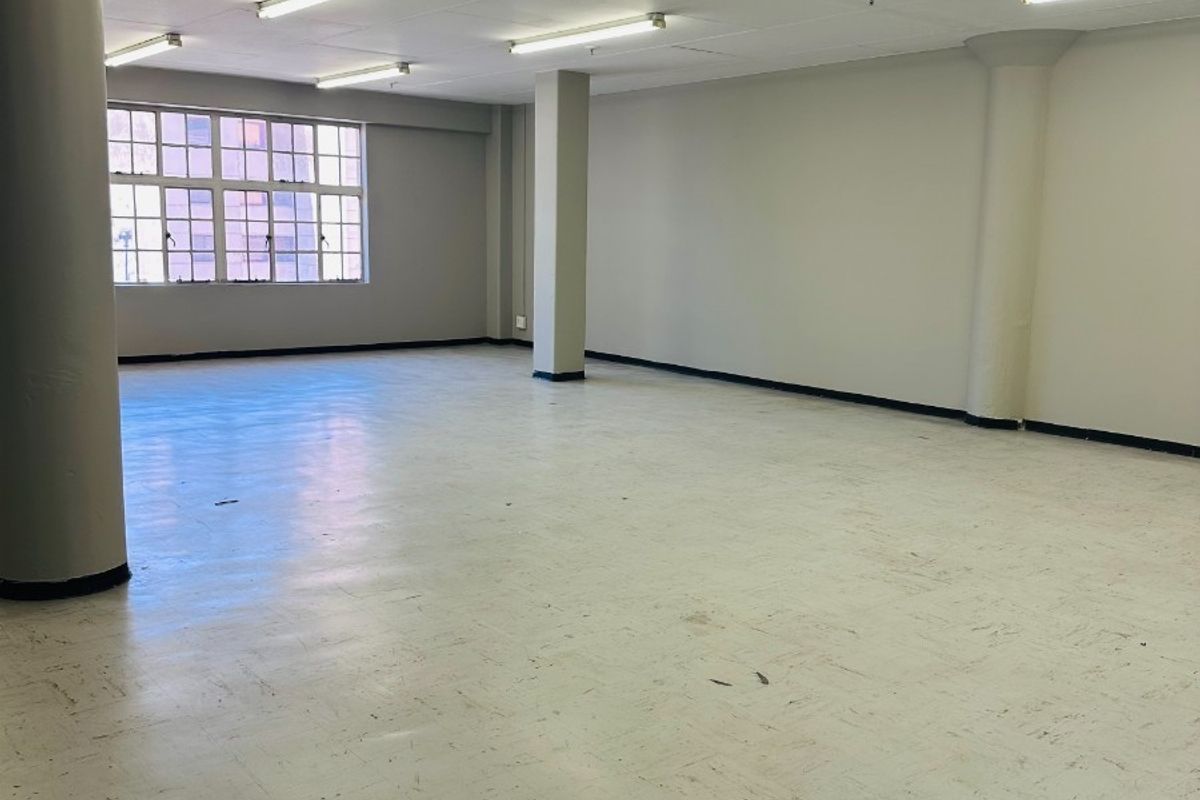 Spacious open-plan commercial office area featuring structural columns, vinyl flooring, and fluorescent lighting, offering a versatile blank canvas for various business configurations.