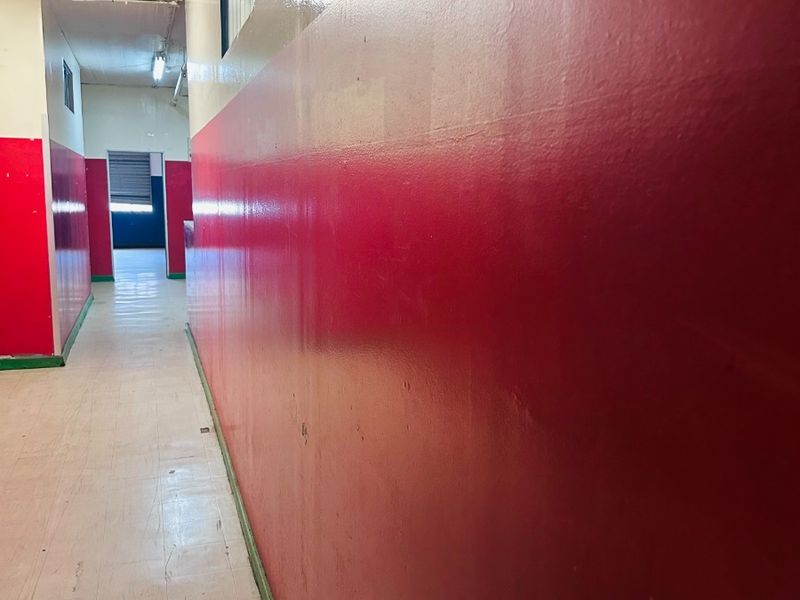 A long, empty commercial hallway featuring high-contrast red and cream painted walls and durable vinyl flooring.