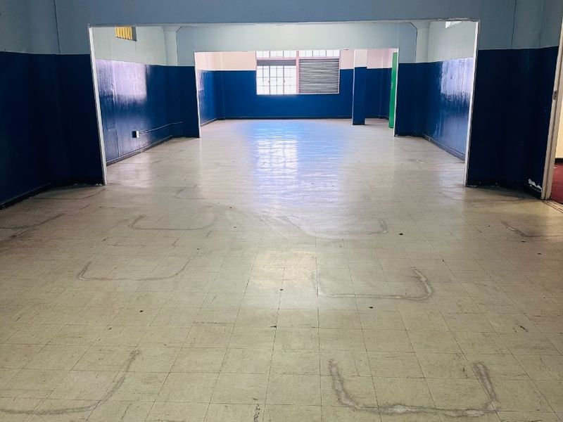A large, vacant open-plan commercial space featuring vinyl tile flooring, dual-tone painted walls, and natural light from rear windows.
