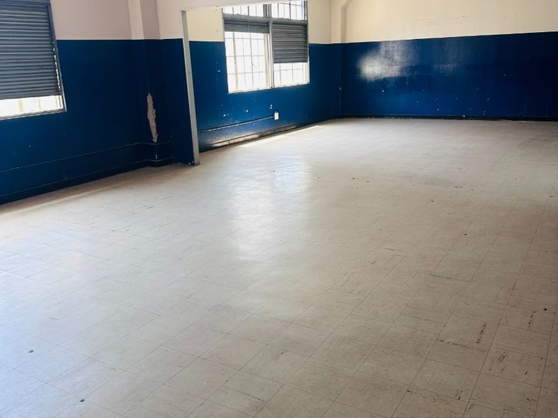 Spacious open-plan commercial area featuring vinyl tile flooring, exposed ceiling pipes, and large multi-pane windows, offering a versatile layout for various business needs.