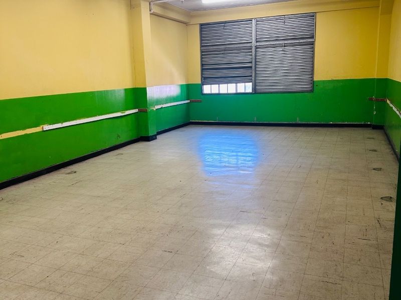 An empty office space featuring vinyl tile flooring, exposed ceiling beams, and louvered windows, ready for renovation or commercial fit-out.