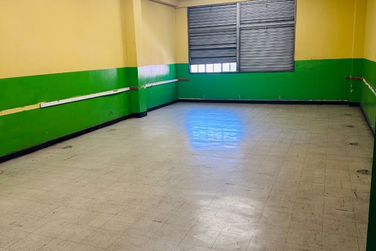 An empty office space featuring vinyl tile flooring, exposed ceiling beams, and louvered windows, ready for renovation or commercial fit-out.
