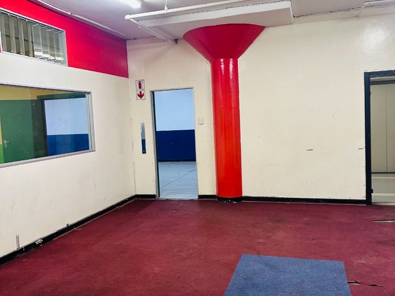 An empty office space featuring a prominent red structural column, fluorescent lighting, and worn carpet flooring, suitable for commercial renovation or workspace reconfiguration.
