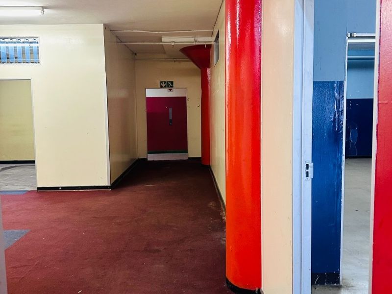 An empty commercial hallway featuring structural columns, red carpeting, and access to adjacent rooms through multiple doorways.