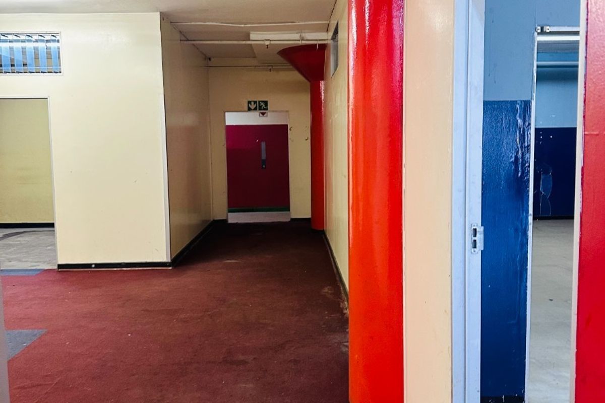 An empty commercial hallway featuring structural columns, red carpeting, and access to adjacent rooms through multiple doorways.