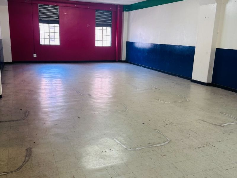 A spacious, open-plan commercial area featuring exposed concrete ceilings, fluorescent lighting, and vinyl tile flooring, suitable for various business or office configurations.