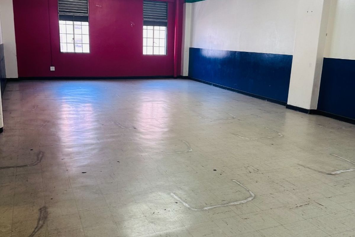 A spacious, open-plan commercial area featuring exposed concrete ceilings, fluorescent lighting, and vinyl tile flooring, suitable for various business or office configurations.