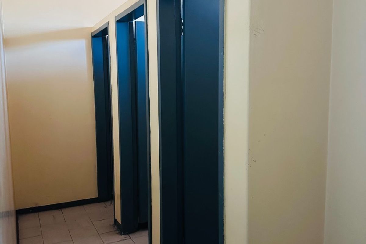 A functional commercial bathroom area featuring multiple partitioned cubicles, tiled flooring, and basic overhead lighting.