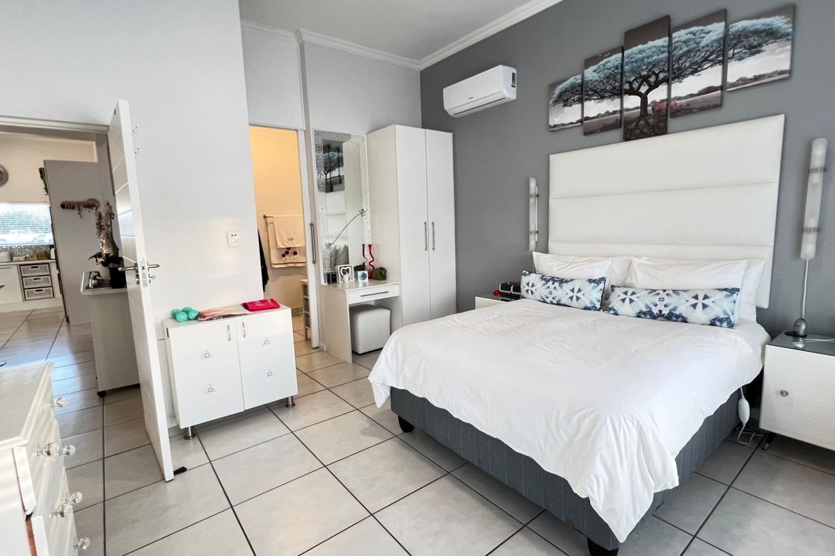 Spacious bedroom featuring tiled flooring, a wall-mounted air conditioning unit, and direct access to an en-suite bathroom.