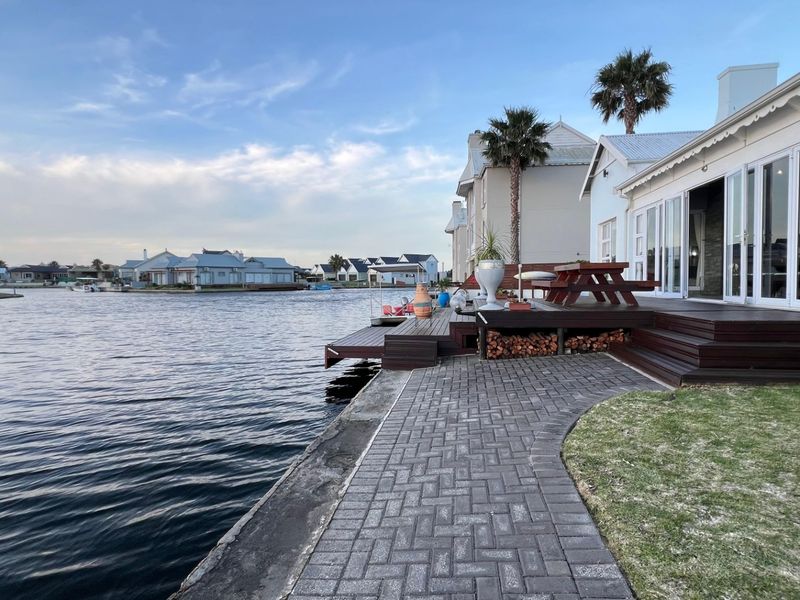 Waterfront patio area featuring timber decking, paved pathways, and direct access to the canal, complemented by large bi-fold doors leading into the home.