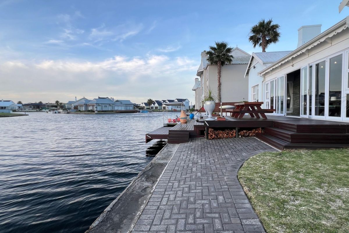 Waterfront patio area featuring timber decking, paved pathways, and direct access to the canal, complemented by large bi-fold doors leading into the home.