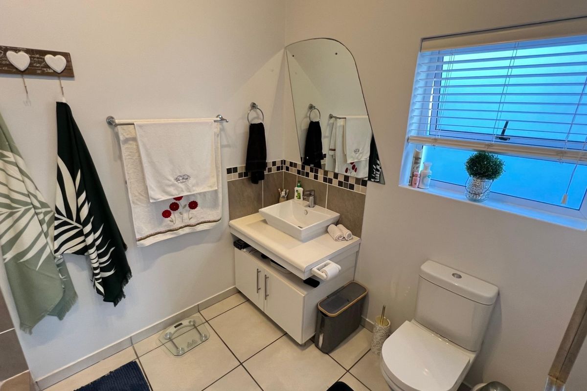 A functional bathroom featuring a modern vessel sink on a vanity cabinet, tiled backsplash, toilet, and a window with fitted blinds.