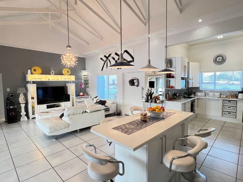 Spacious open-plan living area featuring a vaulted ceiling with exposed rafters, a modern kitchen with a central island, and bright tiled flooring throughout.