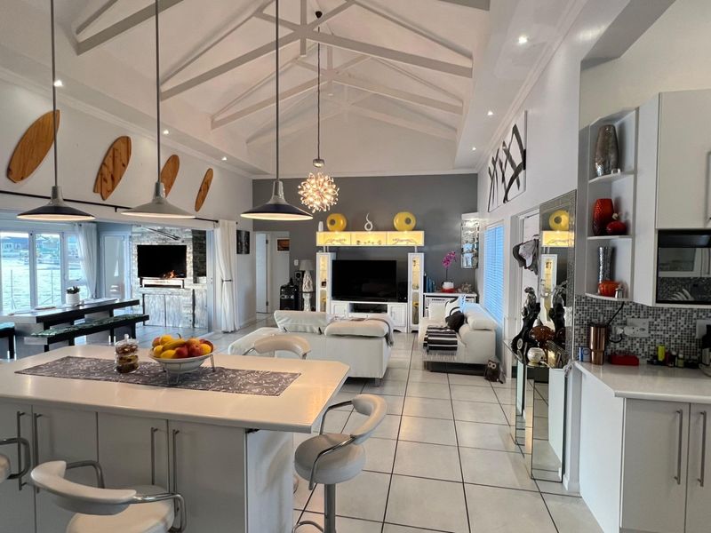 Spacious open-plan living area featuring a vaulted ceiling with exposed trusses, a modern kitchen island, and seamless flow to the outdoor patio area.