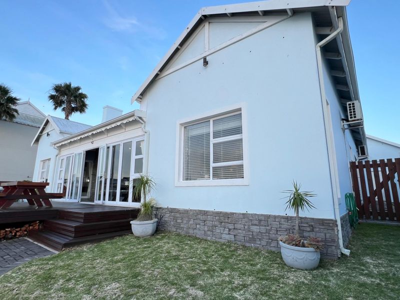 Rear view of the house featuring a timber deck, sliding glass doors, stone cladding base, and a well-maintained garden area.