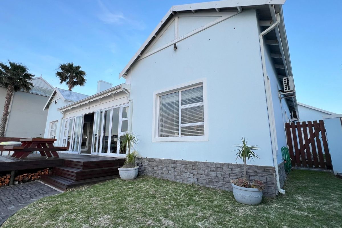 Rear view of the house featuring a timber deck, sliding glass doors, stone cladding base, and a well-maintained garden area.