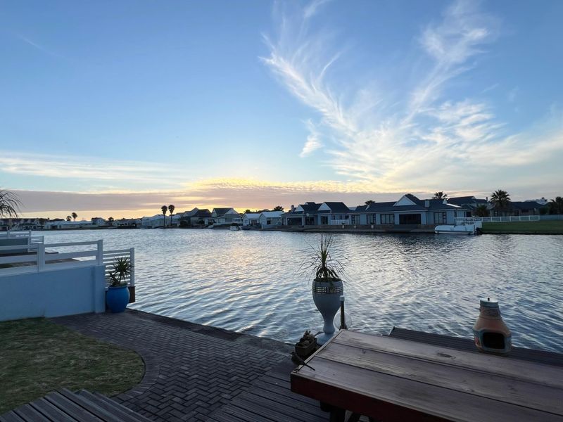 A scenic waterfront view overlooking a canal with surrounding residential properties, featuring a paved patio area and direct water access.