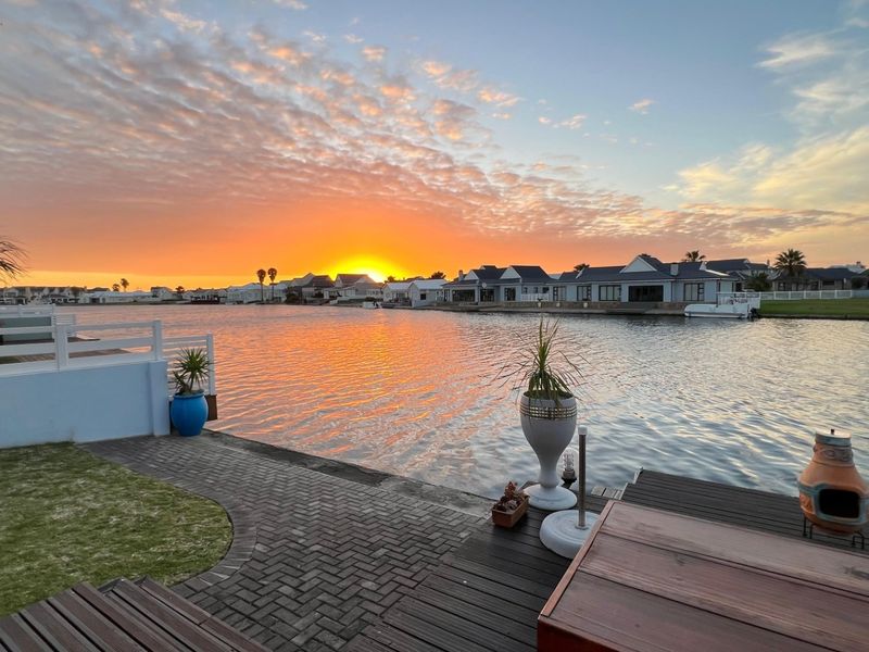 A scenic sunset view over the waterfront, featuring a paved patio area, timber decking, and direct access to the canal.