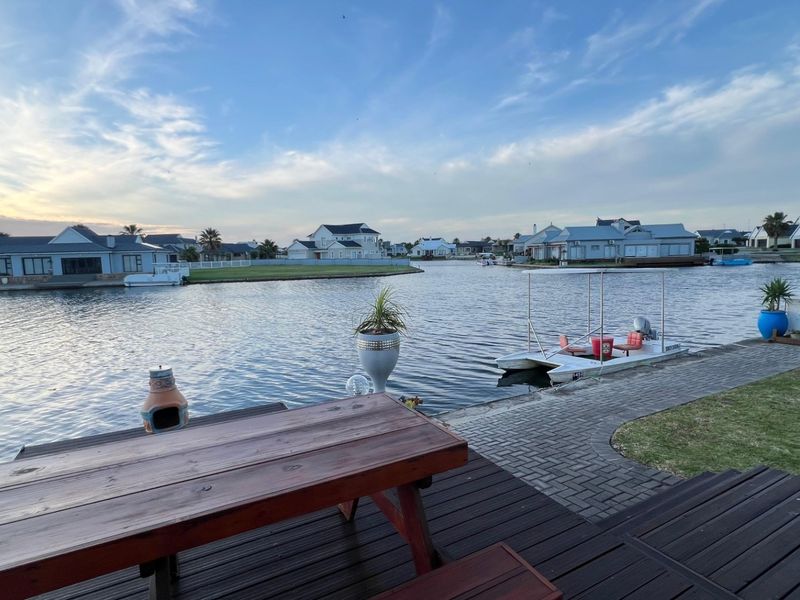 A scenic waterfront view from a timber deck, overlooking a canal with surrounding residential properties and private boat access.